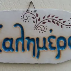 Ceramiczna tabliczka z napisem "Καλημέρα" (Dzień dobry) po grecku, ozdobiona roślinnym motywem.
