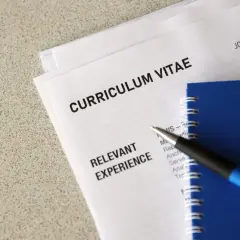 Długopis leży na dokumentach z nagłówkiem "CURRICULUM VITAE". Widoczna jest sekcja "RELEVANT EXPERIENCE" oraz klauzula CV po angielsku.