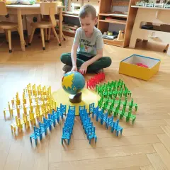 Chłopiec bawi się klockami w kształcie krzesełek, tworząc okręgi wokół globusa. To nauka przez zabawę w stylu metoda montessori.
