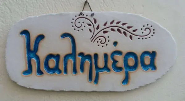 Ceramiczna tabliczka z napisem "Καλημέρα" (Dzień dobry) po grecku, ozdobiona roślinnym motywem.