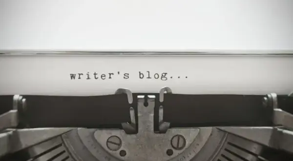 Maszyna do pisania z napisem "writer's blog...". Zastanawiasz się, jak napisać bloga po angielsku? Zacznij od tego!