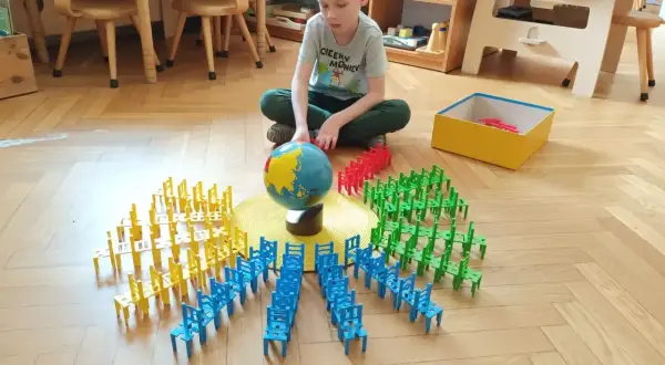 Chłopiec bawi się klockami w kształcie krzesełek, tworząc okręgi wokół globusa. To nauka przez zabawę w stylu metoda montessori.