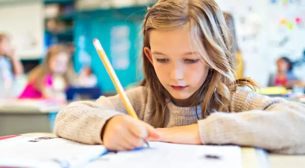 Dziewczynka skupiona na nauce, pisze w zeszycie. Czy jest obowiązek nauki do 18 roku życia? Tak, edukacja jest ważna!
