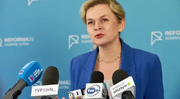 Kobieta w niebieskiej marynarce przemawia do mediów, omawiając zmiany w karcie nauczyciela.