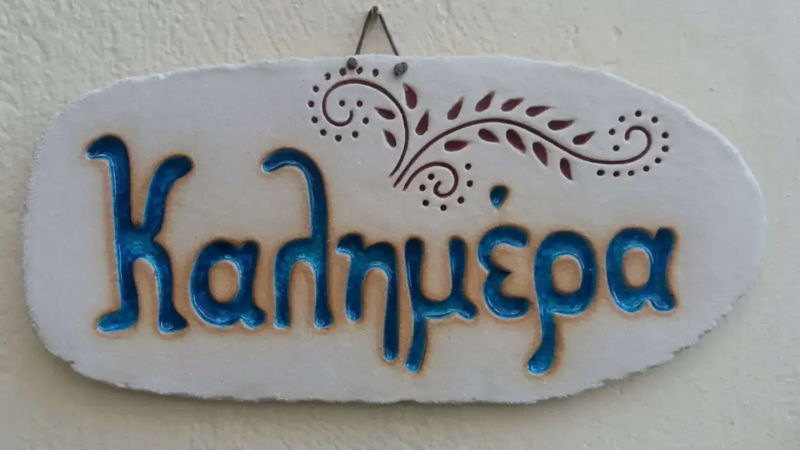 Ceramiczna tabliczka z napisem "Καλημέρα" (Dzień dobry) po grecku, ozdobiona roślinnym motywem.