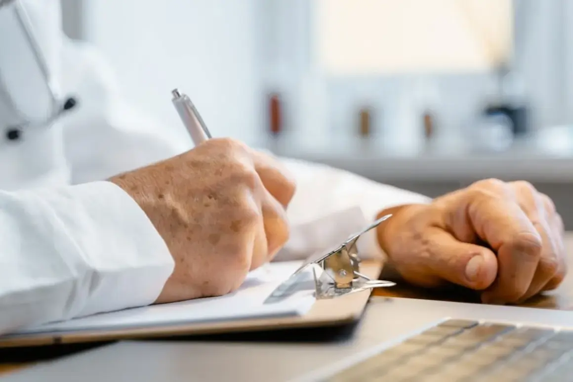 Doktor nauk medycznych w białym kitlu notuje informacje na kartce.