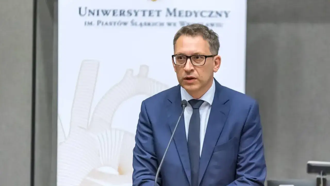 Doktor nauk medycznych w garniturze przemawia na tle Uniwersytetu Medycznego.
